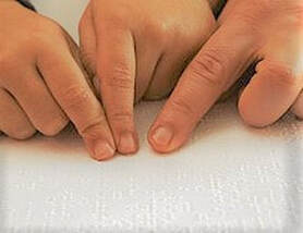 Fotografia a 3 dedos sobre folha branca com texto braille